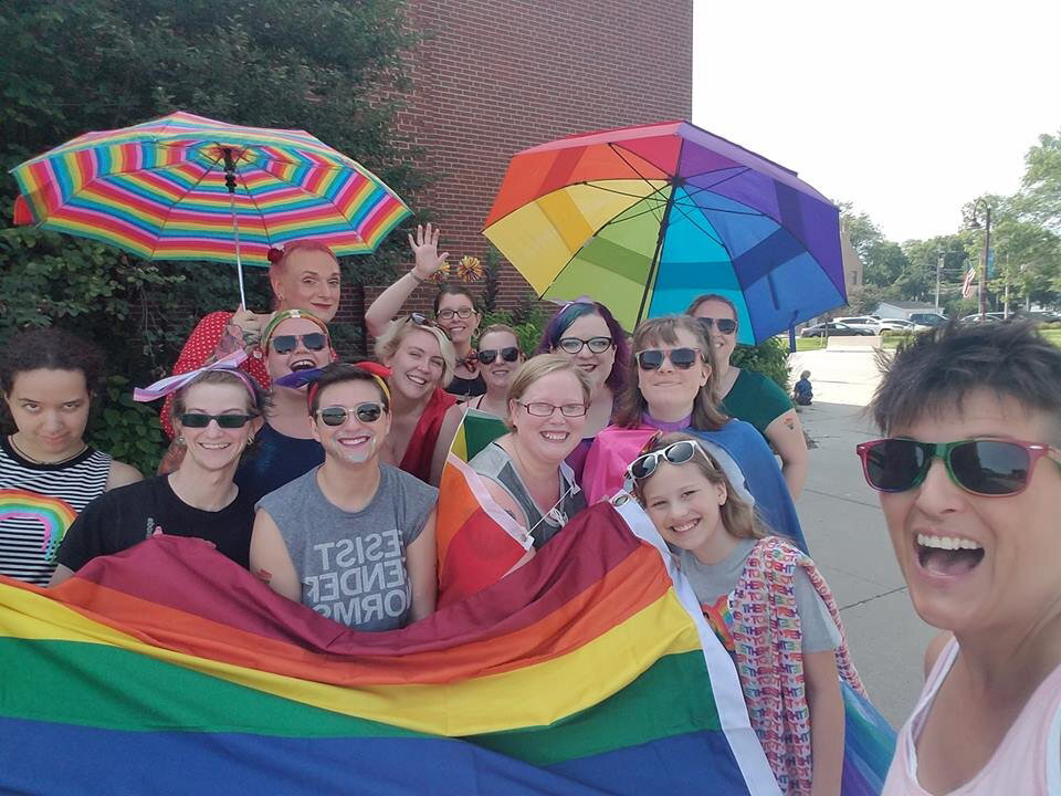 A group of people with rainbow colored flag, umbrellas, and apparel at a Pride event
