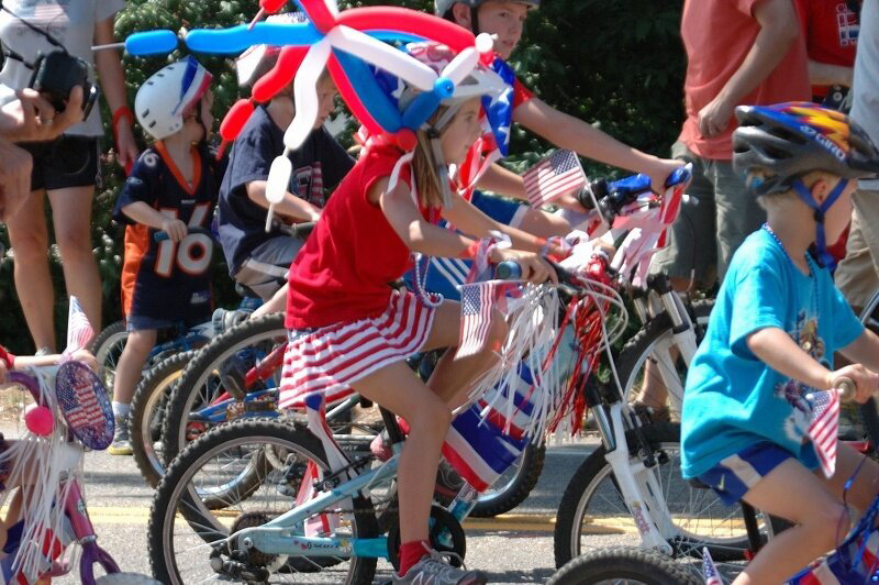 Kids riding bikes decked out with American flags and red white and blue