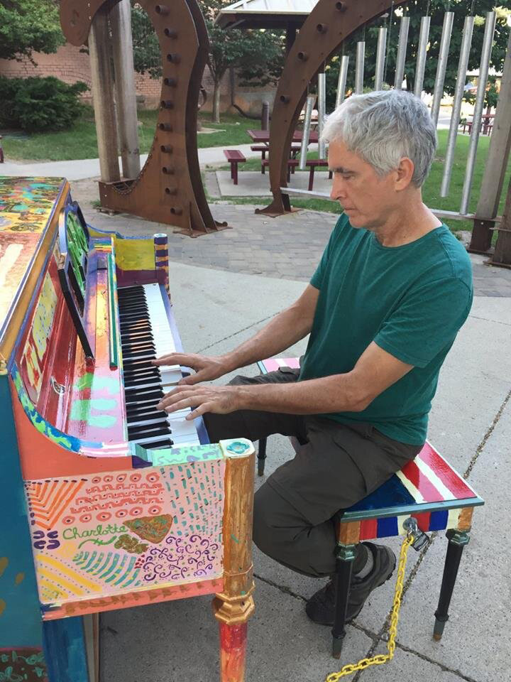 A man playing a brightly painted piano in Downtown Ames